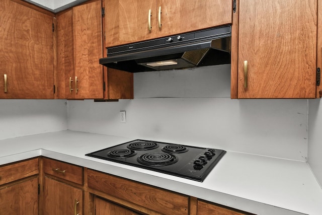 kitchen featuring under cabinet range hood, brown cabinetry, black electric stovetop, and light countertops
