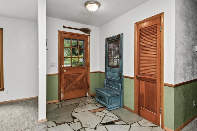 entryway featuring a textured ceiling, baseboards, and a textured wall