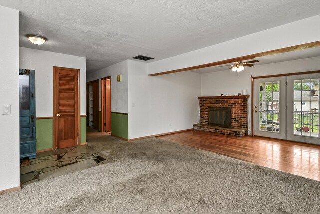 unfurnished living room featuring ceiling fan, a brick fireplace, carpet, baseboards, and visible vents