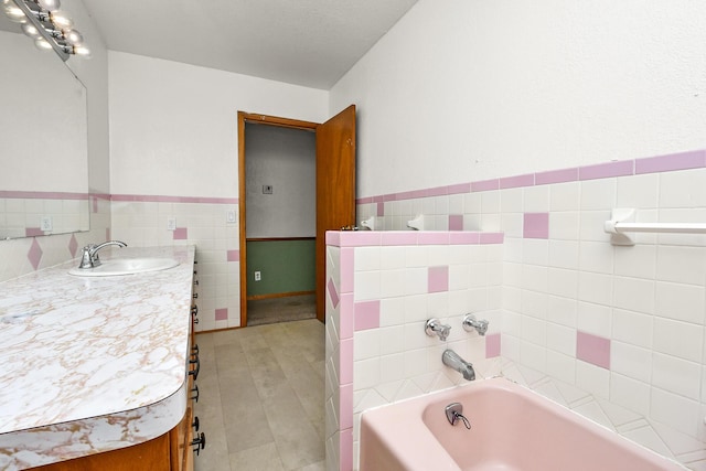 full bath with vanity, tile walls, a garden tub, and a wainscoted wall