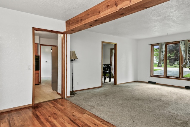 spare room with baseboards, carpet flooring, a textured ceiling, and wood finished floors