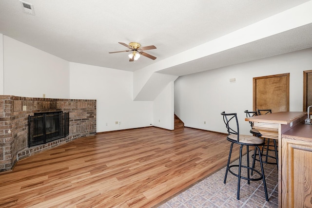 interior space with visible vents, a brick fireplace, light wood-style floors, baseboards, and a ceiling fan