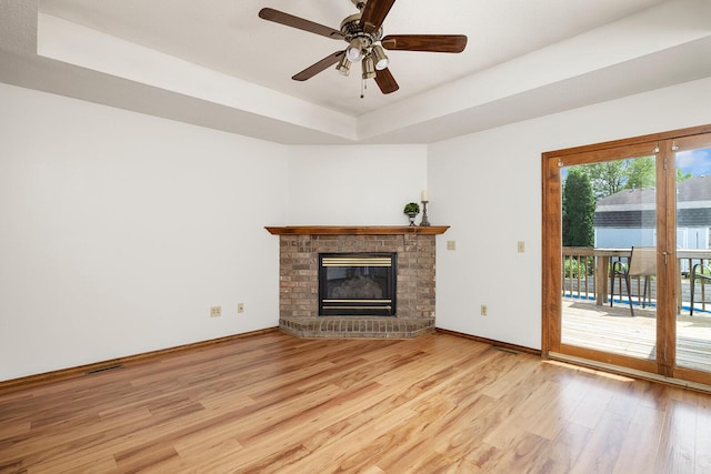 unfurnished living room featuring visible vents, wood finished floors, a fireplace, baseboards, and a raised ceiling