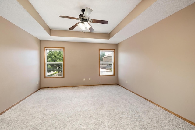 spare room featuring a ceiling fan, a tray ceiling, light colored carpet, and baseboards