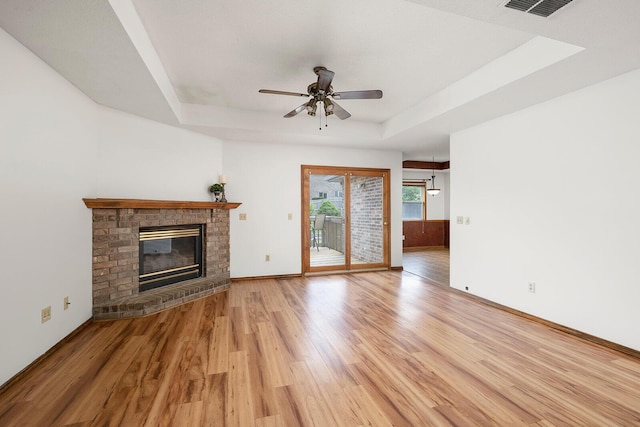 unfurnished living room with a fireplace, a ceiling fan, a tray ceiling, and light wood-type flooring