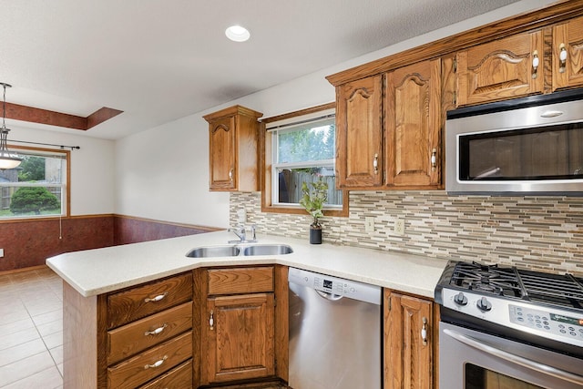 kitchen with stainless steel appliances, brown cabinetry, a sink, and a peninsula