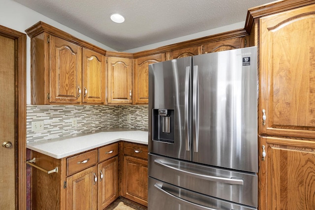 kitchen featuring light countertops, brown cabinetry, stainless steel fridge, and tasteful backsplash
