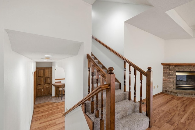 staircase featuring baseboards, a brick fireplace, and wood finished floors