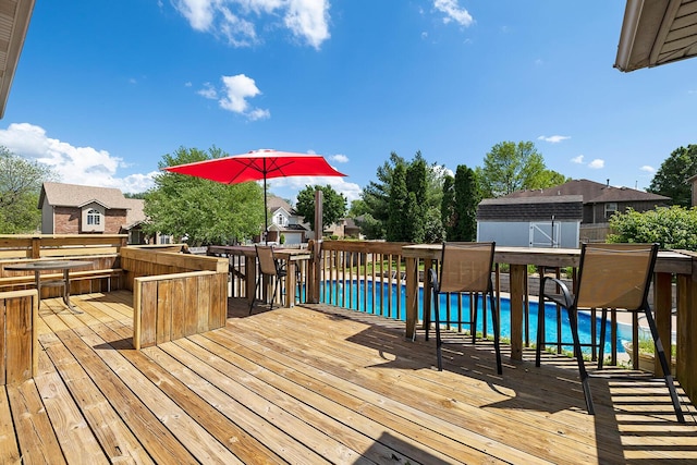 wooden deck featuring a storage unit, an outdoor pool, an outbuilding, and outdoor dining space