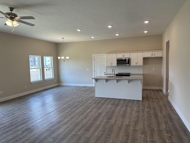 kitchen with an island with sink, dark wood-type flooring, white cabinetry, stainless steel microwave, and a sink