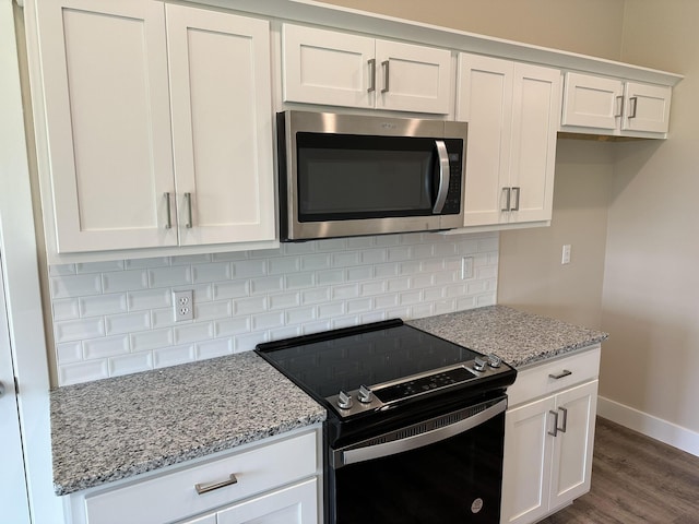 kitchen with baseboards, black range with electric cooktop, stainless steel microwave, and white cabinetry