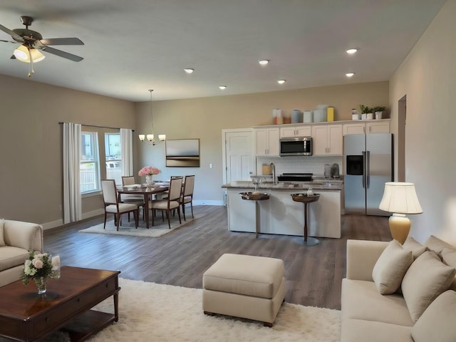 living area featuring recessed lighting, baseboards, dark wood-style floors, and ceiling fan with notable chandelier