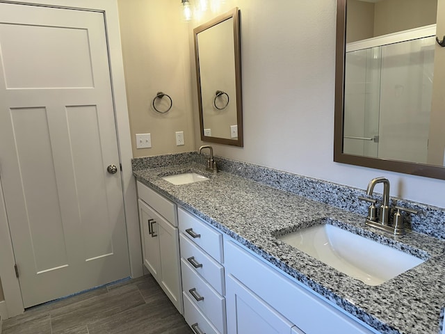full bathroom with double vanity, a sink, a shower with shower door, and wood finished floors