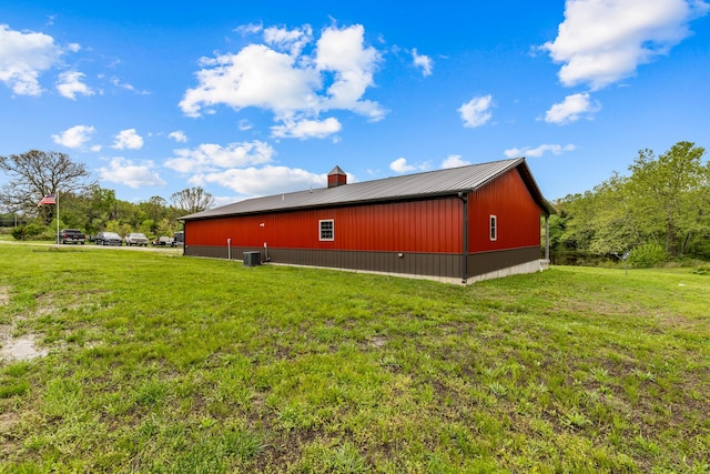 view of side of home featuring central air condition unit, an outbuilding, a yard, and metal roof