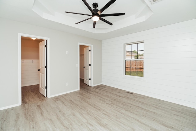 unfurnished bedroom with ceiling fan, a raised ceiling, baseboards, light wood-type flooring, and a spacious closet