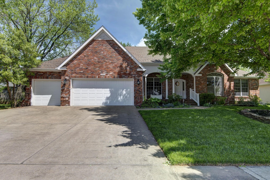 view of front of house with brick siding, an attached garage, driveway, and a front yard