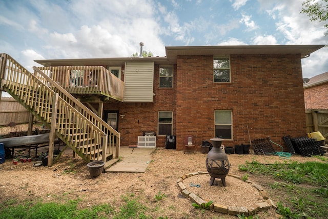 rear view of house with a fire pit, fence, a deck, brick siding, and stairway