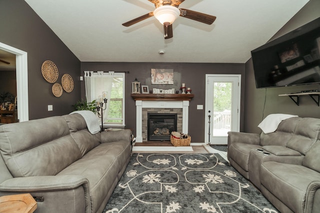 living room featuring ceiling fan, vaulted ceiling, a stone fireplace, and wood finished floors