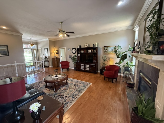 living area with wood finished floors, ornamental molding, a fireplace, ceiling fan, and baseboards