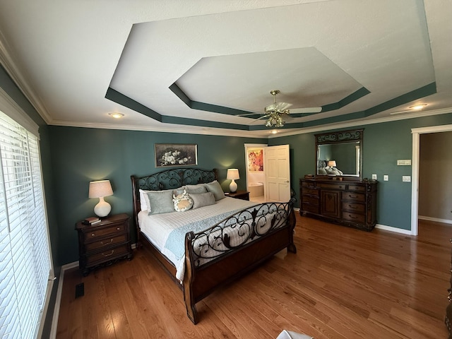 bedroom featuring wood finished floors, visible vents, crown molding, a tray ceiling, and baseboards