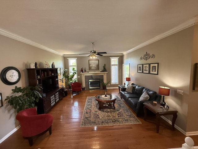 living area with crown molding, wood finished floors, baseboards, and a ceiling fan