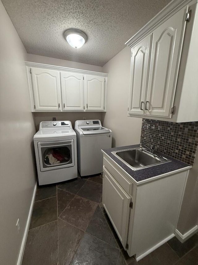 washroom with a textured ceiling, cabinet space, a sink, and washer and clothes dryer