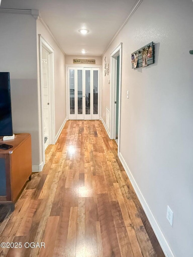corridor featuring crown molding, baseboards, french doors, and light wood finished floors