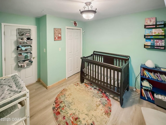 bedroom with baseboards, a crib, and wood finished floors