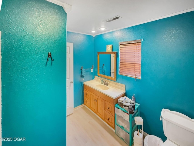 half bath with crown molding, wood finished floors, vanity, toilet, and a textured wall