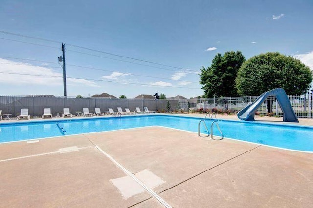 community pool with fence, a water slide, and a patio