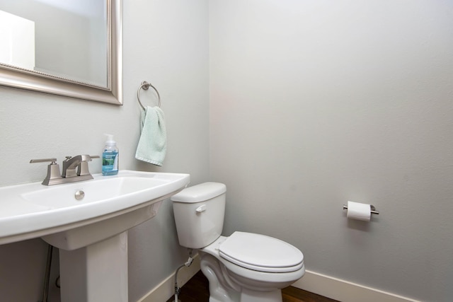half bathroom with baseboards, wood finished floors, and toilet