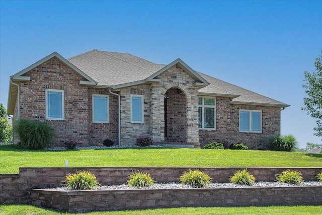 view of front of property featuring brick siding, roof with shingles, and a front yard