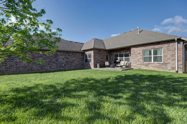 back of property with a lawn, a patio, brick siding, and roof with shingles