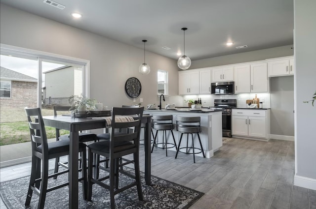kitchen with dark countertops, appliances with stainless steel finishes, white cabinetry, backsplash, and visible vents