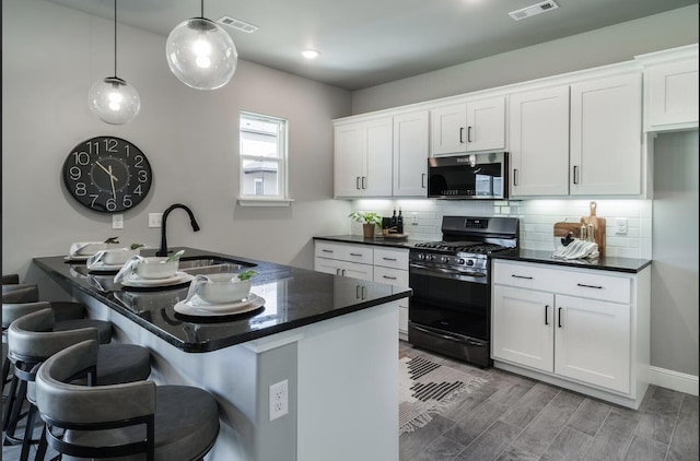 kitchen with tasteful backsplash, a sink, black gas range oven, stainless steel microwave, and white cabinets