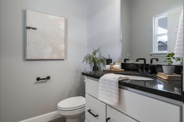 half bath featuring vanity, baseboards, and toilet