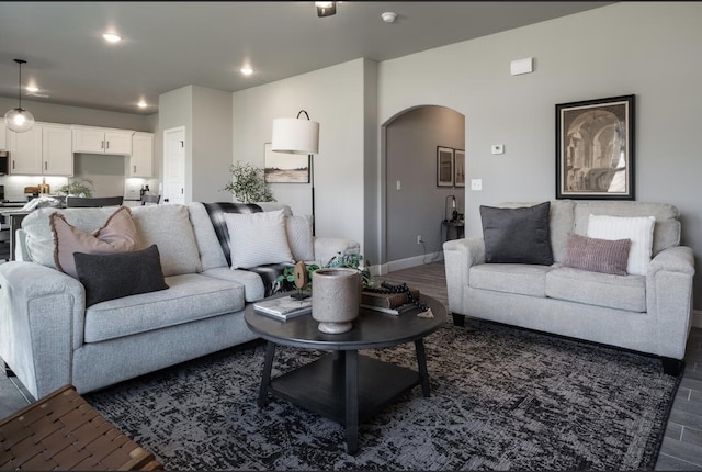 living area featuring arched walkways, baseboards, dark wood-style flooring, and recessed lighting
