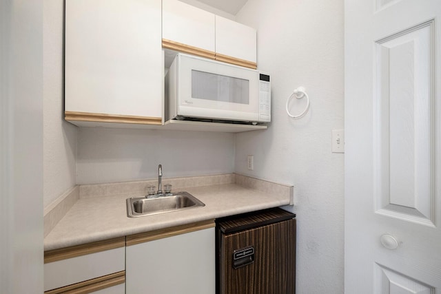 kitchen with a sink, white cabinetry, white microwave, and light countertops