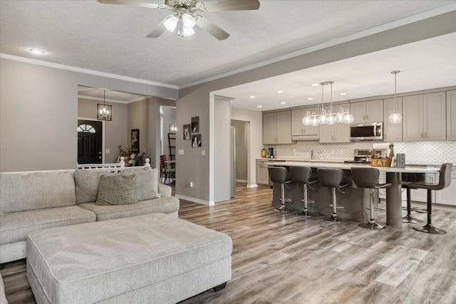 living area featuring a textured ceiling, ceiling fan, ornamental molding, and light wood-style flooring