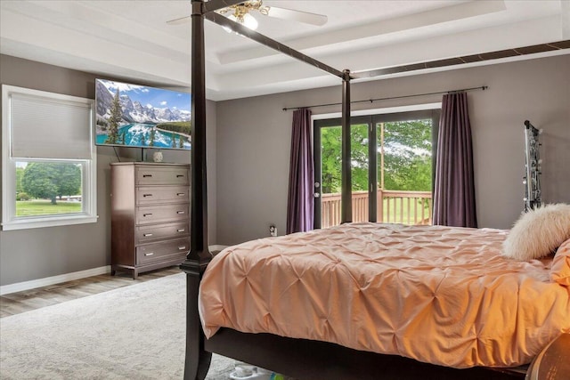 bedroom featuring wood finished floors, access to exterior, baseboards, a tray ceiling, and a ceiling fan