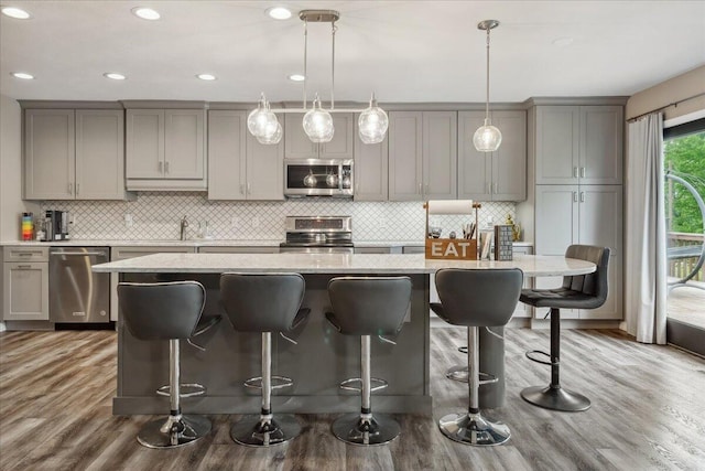 kitchen featuring a breakfast bar area, gray cabinets, stainless steel appliances, decorative backsplash, and wood finished floors