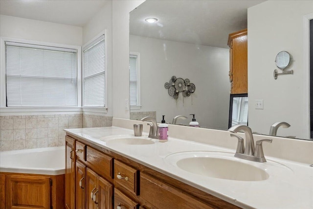 bathroom with double vanity, a sink, a bath, and a healthy amount of sunlight
