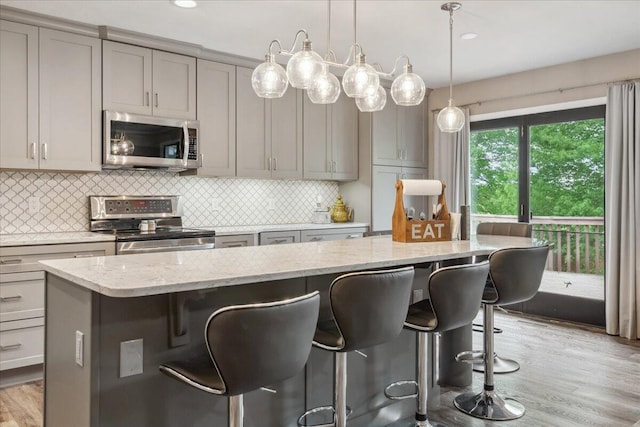kitchen with gray cabinets, a kitchen breakfast bar, appliances with stainless steel finishes, tasteful backsplash, and light stone counters