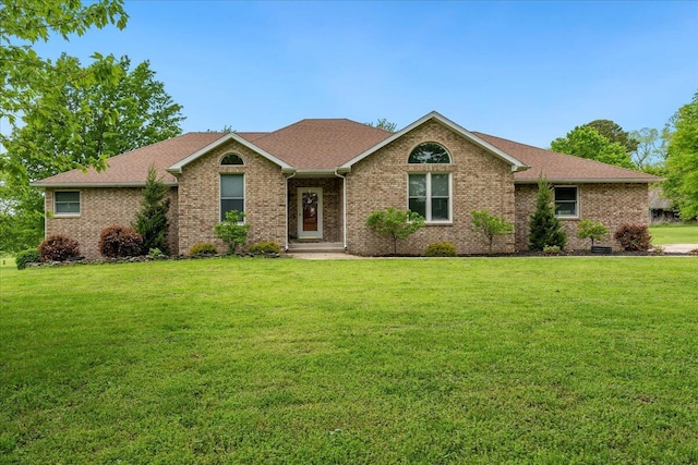 ranch-style home featuring brick siding, a front yard, and roof with shingles