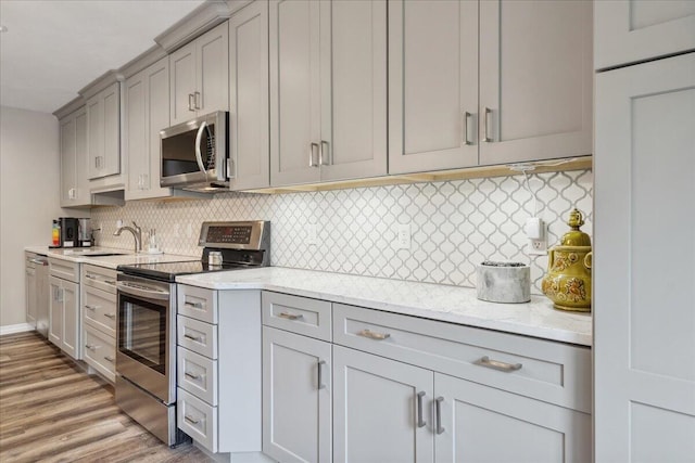 kitchen with tasteful backsplash, light wood-type flooring, gray cabinetry, light stone counters, and stainless steel appliances