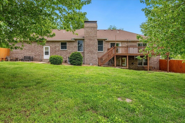 back of property featuring fence, a deck, stairway, a chimney, and a lawn