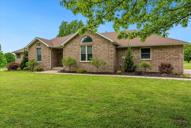 ranch-style home featuring a shingled roof, a front yard, and brick siding