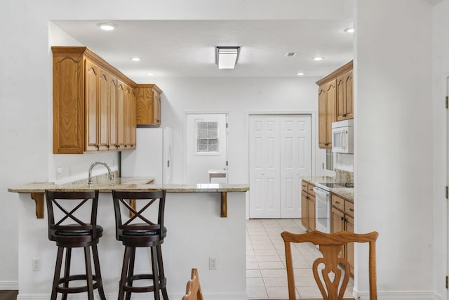 kitchen with a peninsula, a breakfast bar area, white appliances, and light stone countertops