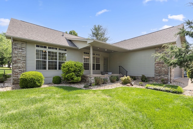 back of house with a lawn, a garage, roof with shingles, and brick siding