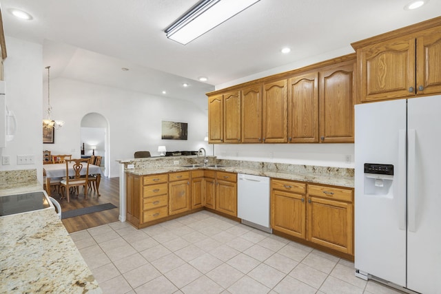 kitchen with a peninsula, white appliances, arched walkways, brown cabinets, and a sink